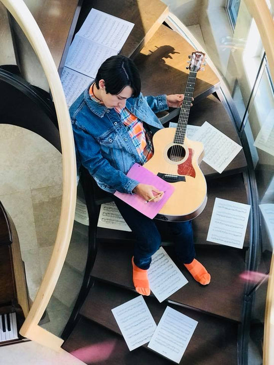 Justin Riverstone on staircase with guitar and papers all around him