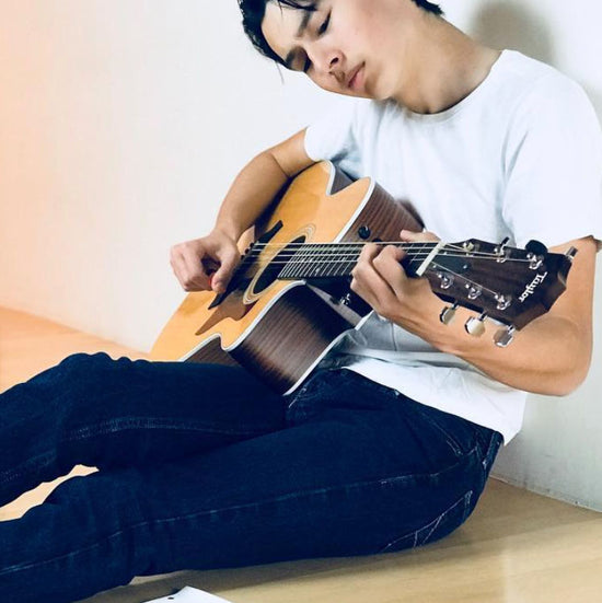 Justin Riverstone sitting on floor playing guitar